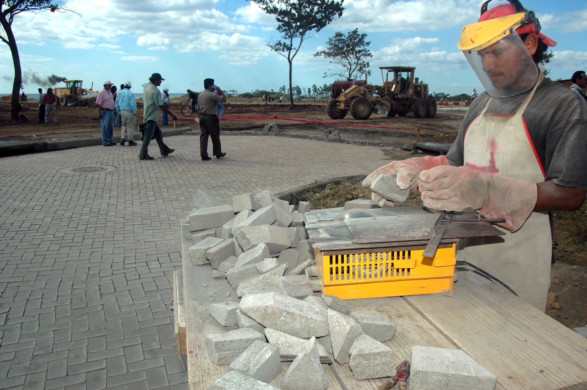 A mason cutting paving stones on a jobsite as roadwork goes on behind him